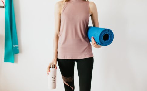 crop sportswoman carrying sport mat and bottle of water before exercising